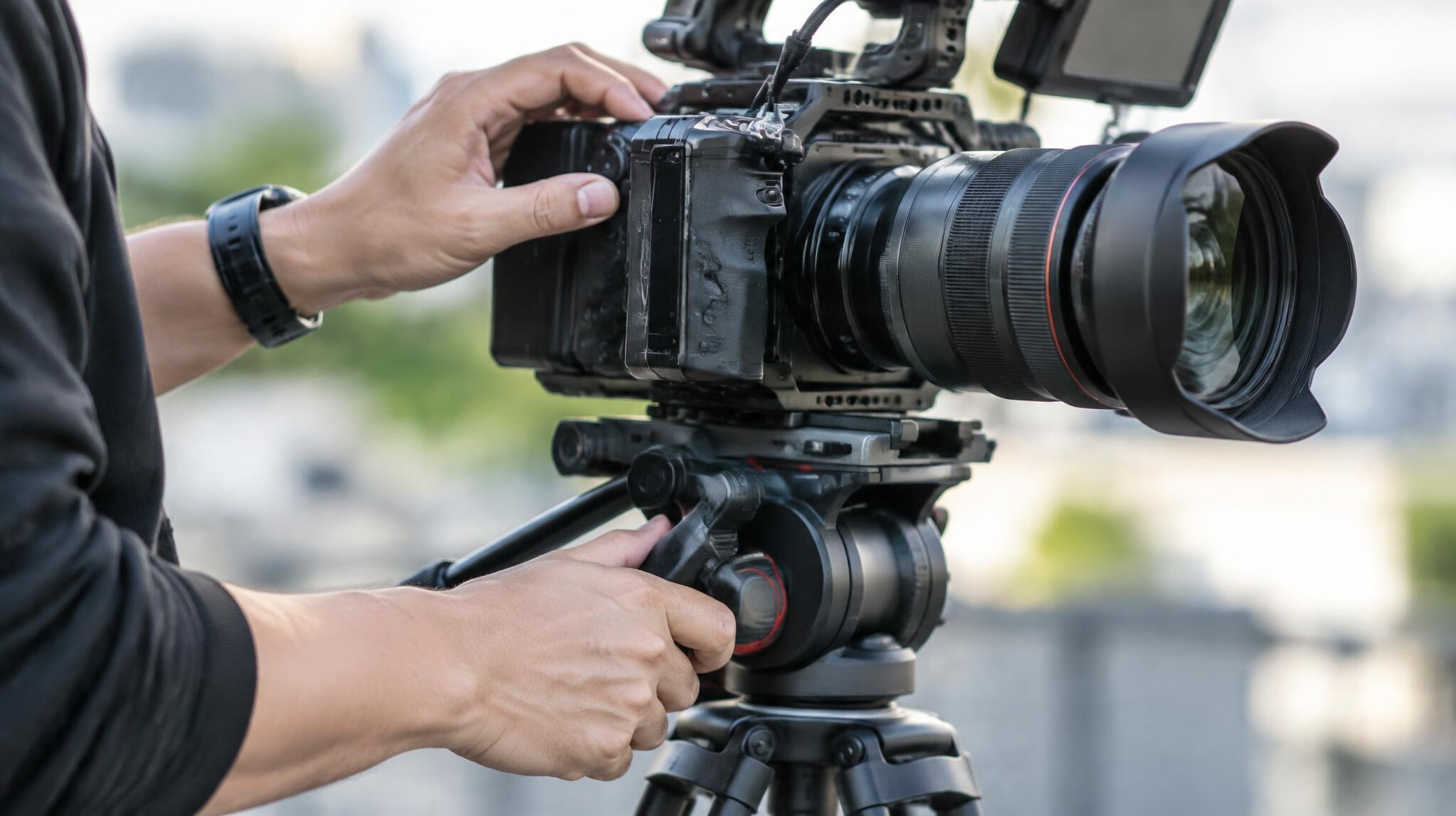 Camera operator's hands adjusting a camera on a tripod